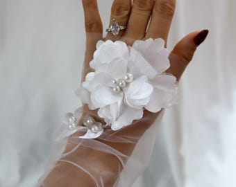 May include: White tulle gloves with a floral design and pearl accents. The gloves are sheer and delicate, with a cluster of white flowers on the back of the hand.