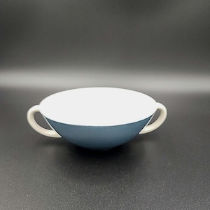 May include: A white and blue ceramic bowl with two handles. The bowl is round and has a slight curve to it. The bowl is ideal for serving soup or cereal.