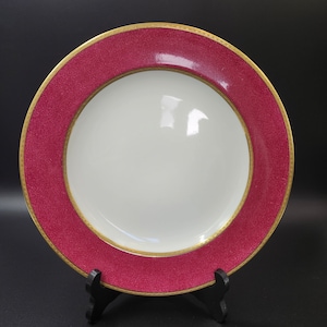 May include: A large, round, pink dinner plate with a gold rim. The plate has a white centre and is perfect for serving a meal.
