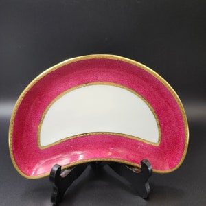 May include: A half-moon shaped serving dish with a white center and a deep pink rim with a gold trim.