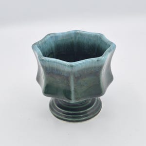 May include: A ceramic pedestal bowl featuring a scalloped, eight-sided rim. The glaze transitions from a deep, dark forest green at the base and body to a lighter, vibrant turquoise blue along the upper edges and rim, creating a smooth gradient.