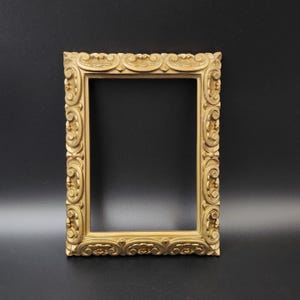Puede incluir: Un marco de fotos de color dorado con un diseño ornamentado. El marco está hecho de madera y tiene una forma rectangular.
