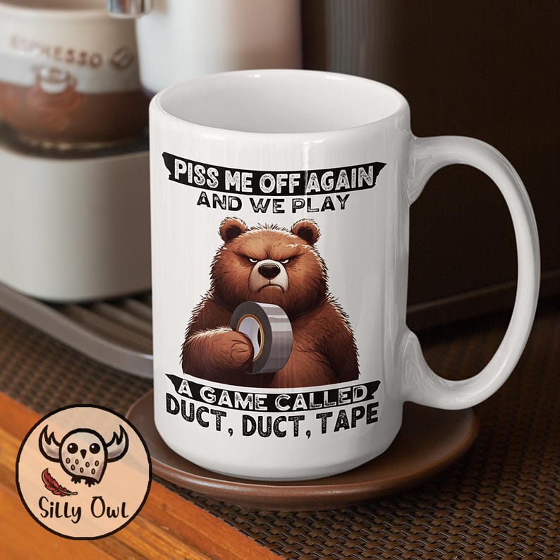 A 15oz white ceramic coffee mug featuring a cartoon-style illustration of a grumpy grizzly bear. The mug displays the bold, humorous text: "Piss Me Off Again And We Play A Game Called Duct Duct Tape." The design is printed on both sides, making it perfect for right- or left-handed users. A fun and sarcastic gift for coffee lovers with a wild sense of humor.