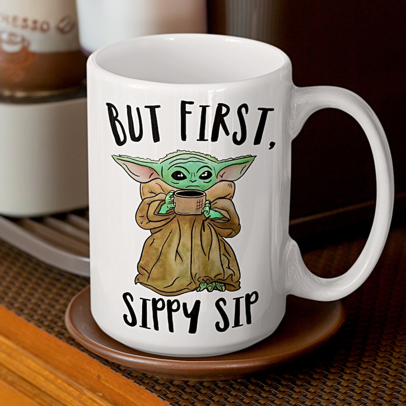 A white ceramic coffee mug featuring a cute illustration of Baby Yoda with the phrase "But First, Sippy Sip." A fun and nerdy mug, perfect for sci-fi fans, coffee lovers, and anyone who needs their caffeine fix before taking on the day.