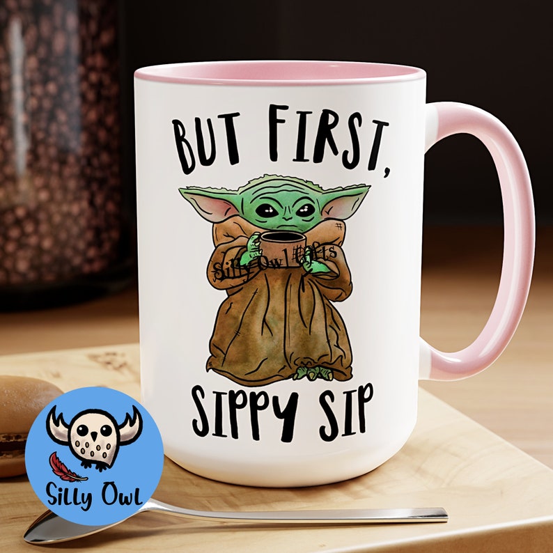 A Pink and White ceramic coffee mug featuring a cute illustration of Baby Yoda with the phrase "But First, Sippy Sip." A fun and nerdy mug, perfect for sci-fi fans, coffee lovers, and anyone who needs their caffeine fix before taking on the day.