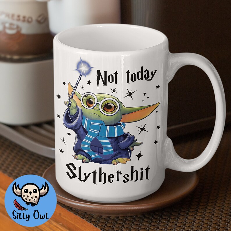 May include: White ceramic mug with a green character holding a wand and wearing glasses. The mug has the text "Not today Slythershit" printed on it.