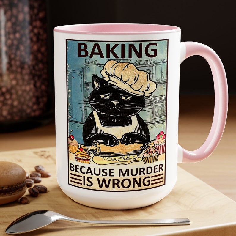 May include: A white ceramic mug with a pink rim features a black cat wearing a chef's hat and rolling out dough. The mug has a vintage-style graphic with the text "Baking because murder is wrong".