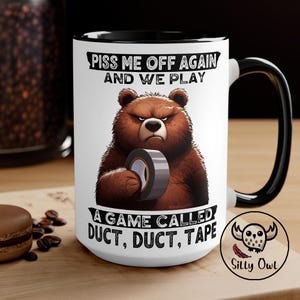 A 15oz black and white ceramic coffee mug featuring a cartoon-style illustration of a grumpy grizzly bear. The mug displays the bold, humorous text: "Piss Me Off Again And We Play A Game Called Duct Duct Tape." The design is printed on both sides, making it perfect for right- or left-handed users. A fun and sarcastic gift for coffee lovers with a wild sense of humor.
