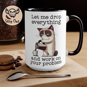 May include: White ceramic coffee mug with a black rim and handle. The mug features a cartoon image of a grumpy cat pouring coffee from a pot. The text on the mug reads "Let me drop everything and work on your problem."