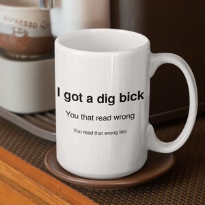 以下が含まれることがあります： 黒い文字で「I got a dig bick You that read wrong You read that wrong too」と書かれた白いセラミック製のコーヒーカップです。