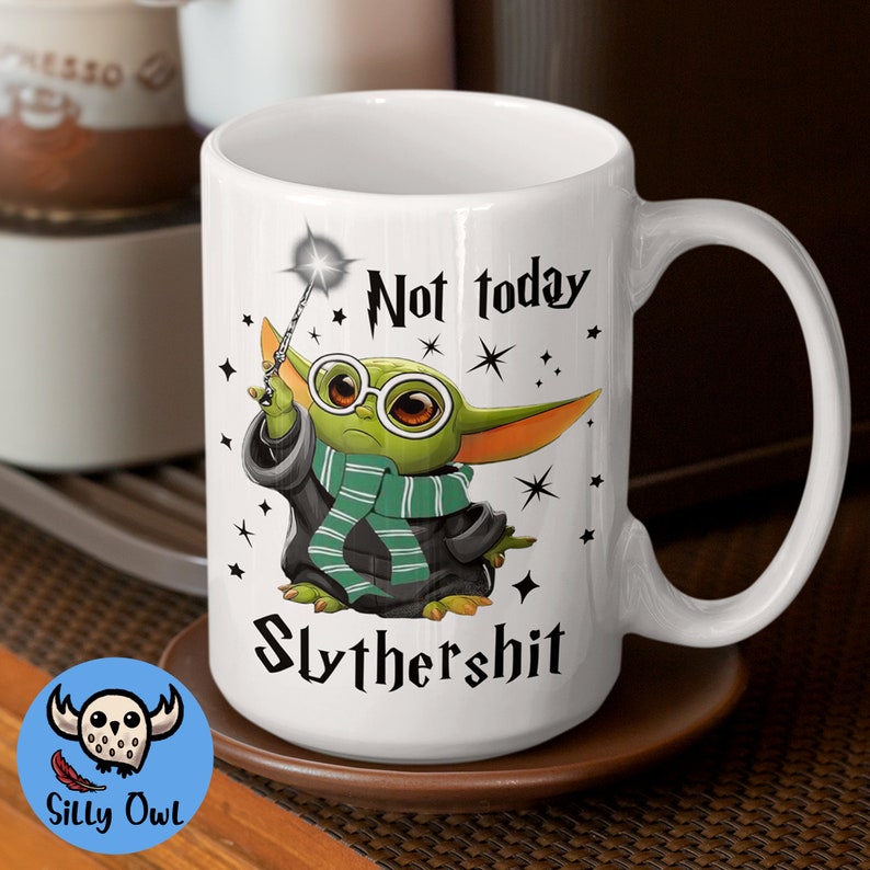 May include: White ceramic mug with a green and black illustration of a baby Yoda character holding a wand. The text "Not today Slythershit" is printed on the mug.