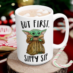 A white ceramic coffee mug featuring a cute illustration of Baby Yoda with the phrase "But First, Sippy Sip." A fun and nerdy mug, perfect for sci-fi fans, coffee lovers, and anyone who needs their caffeine fix before taking on the day.