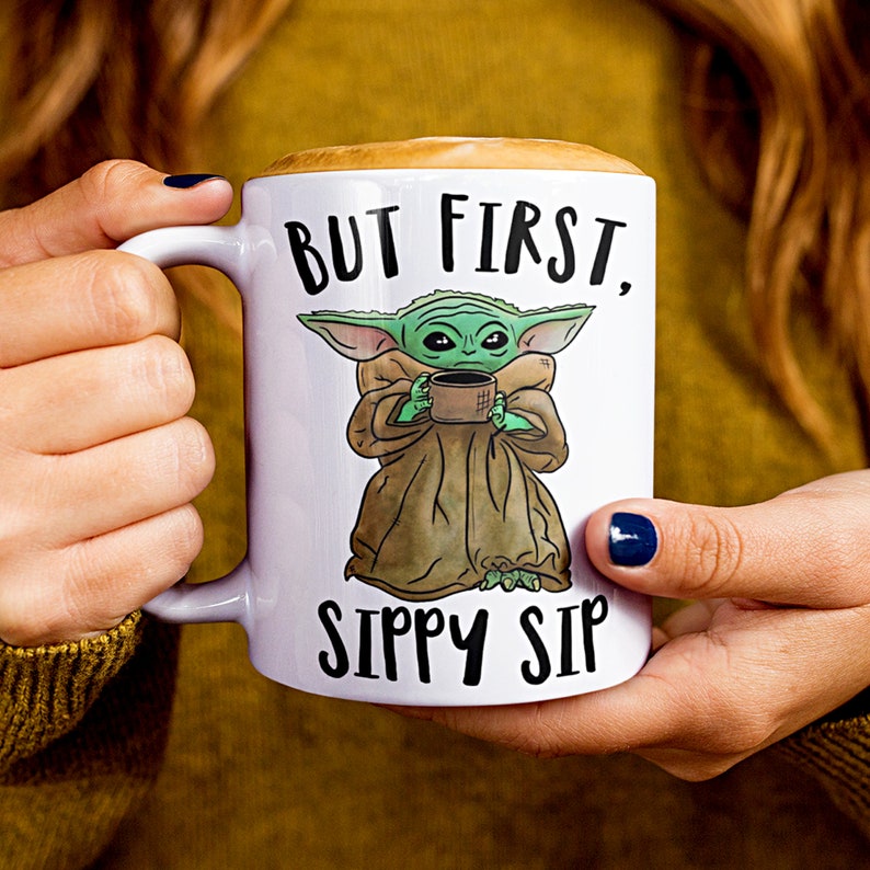 A white ceramic coffee mug featuring a cute illustration of Baby Yoda with the phrase "But First, Sippy Sip." A fun and nerdy mug, perfect for sci-fi fans, coffee lovers, and anyone who needs their caffeine fix before taking on the day.