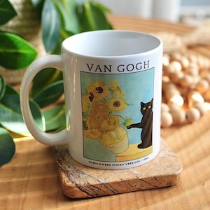 May include: White ceramic mug with a print of Van Gogh's "Sunflowers" painting and a black cat. The mug has a curved handle and sits on a small wooden coaster. The text "VAN GOGH" is printed at the top of the image.