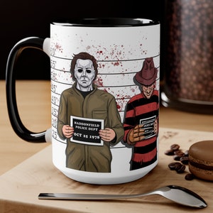 Puede incluir: Taza de cerámica blanca con asa negra. La taza presenta un gráfico de dos personajes de películas de terror, Michael Myers y Freddy Krueger, en una alineación policial. El texto "HADDONFIELD POLICE DEPT OCT 25 1978" está en un cartel que sostiene Michael Myers.