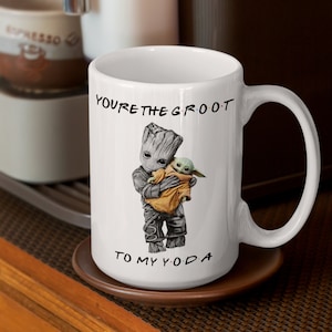 A white ceramic coffee mug featuring an adorable illustration of Groot holding Baby Yoda with the phrase "You're the Groot to My Yoda." A fun and heartwarming sci-fi crossover mug, perfect for best friends, pop culture fans, and geeky coffee lovers.