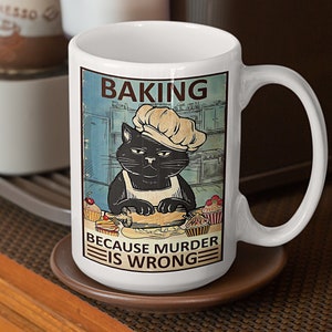 May include: White ceramic mug with a black cat wearing a chef's hat and rolling out dough. The mug has a vintage-style graphic with the text "Baking because murder is wrong".