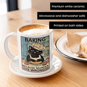 May include: White ceramic coffee mug with a black cat wearing a chef's hat and baking. The mug has the text "Baking because murder is wrong".