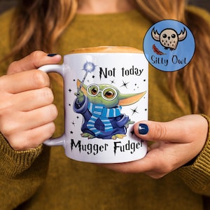 May include: White ceramic mug with a green alien character holding a wand and wearing a blue and white scarf. The mug has the text "Not today Mugger Fudge" printed on it.