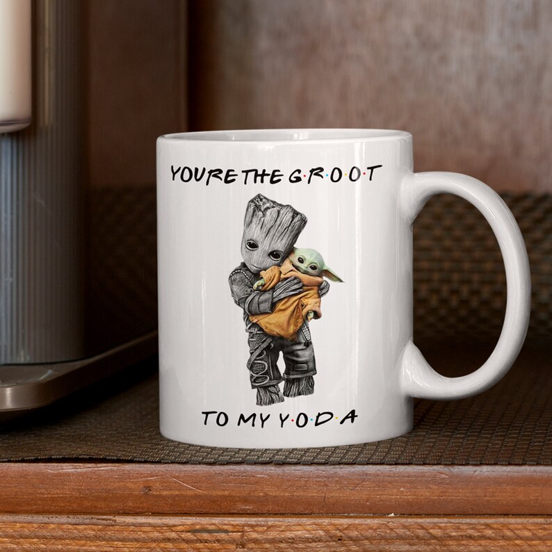 A white ceramic coffee mug featuring an adorable illustration of Groot holding Baby Yoda with the phrase "You're the Groot to My Yoda." A fun and heartwarming sci-fi crossover mug, perfect for best friends, pop culture fans, and geeky coffee lovers.