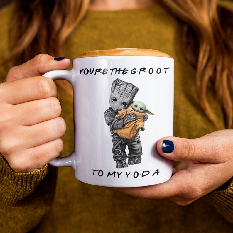 A white ceramic coffee mug featuring an adorable illustration of Groot holding Baby Yoda with the phrase "You're the Groot to My Yoda." A fun and heartwarming sci-fi crossover mug, perfect for best friends, pop culture fans, and geeky coffee lovers.
