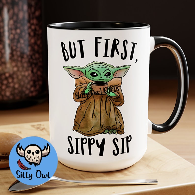 A black and white ceramic coffee mug featuring a cute illustration of Baby Yoda with the phrase "But First, Sippy Sip." A fun and nerdy mug, perfect for sci-fi fans, coffee lovers, and anyone who needs their caffeine fix before taking on the day.