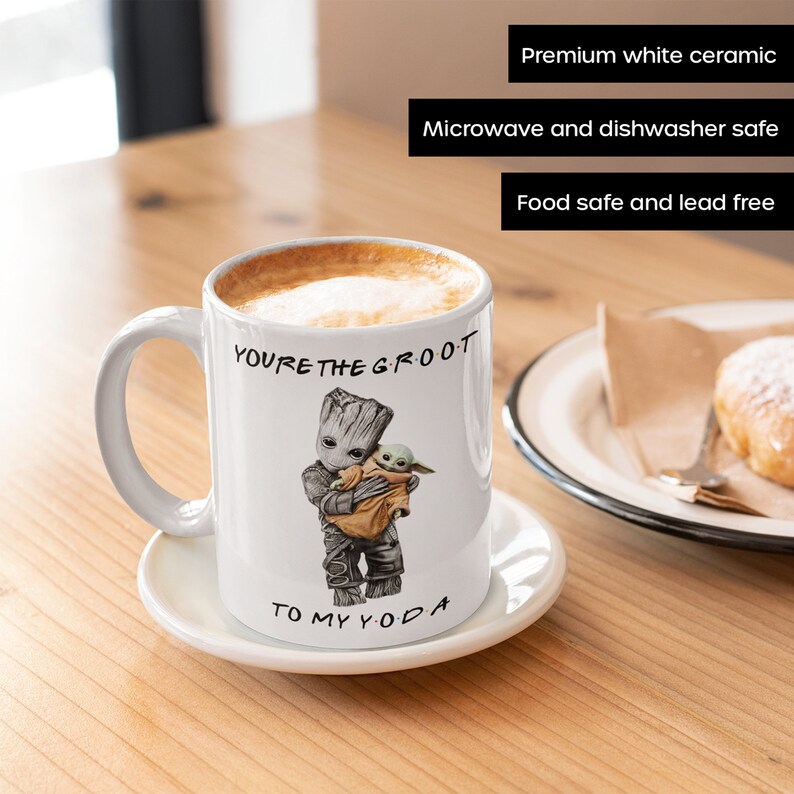 A white ceramic coffee mug featuring an adorable illustration of Groot holding Baby Yoda with the phrase "You're the Groot to My Yoda." A fun and heartwarming sci-fi crossover mug, perfect for best friends, pop culture fans, and geeky coffee lovers.