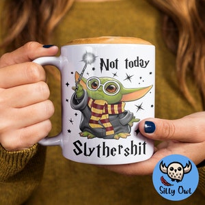 May include: White ceramic mug with a green alien character holding a wand and wearing a Hogwarts house scarf. The mug has the text "Not today Slythershit" printed on it.