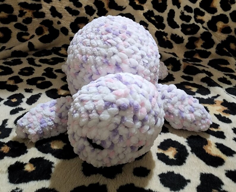 May include: A crocheted plush toy in the shape of a seal. The toy is made with white, pink, and purple yarn and has a black nose.
