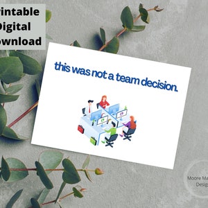 Op de afbeelding: Een witte kaart met de tekst "this was not a team decision" in blauw. De kaart bevat een illustratie van mensen die aan computers werken. De woorden "Printable Digital Download" staan linksboven.