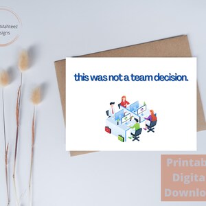 Op de afbeelding: Een witte wenskaart met de tekst "this was not a team decision" in het blauw. De kaart toont een illustratie van vier mensen die aan computers werken. De kaart ligt op een bruine envelop.