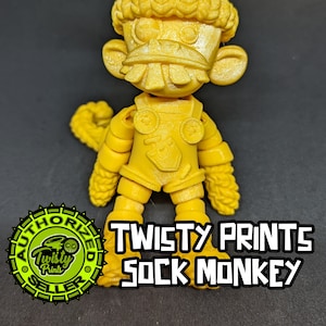 May include: A yellow 3D printed sock monkey toy wearing a Santa hat. The toy has a textured surface and is made of plastic. The toy is standing on a black surface. The text "TWISTY PRINTS SOCK MONKEY" is visible in the image.