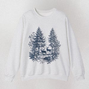 May include: A light gray sweatshirt with a crew neck. The front features a dark blue illustration of two deer in a forest scene with trees. The word "ASH" is printed in the bottom right corner.