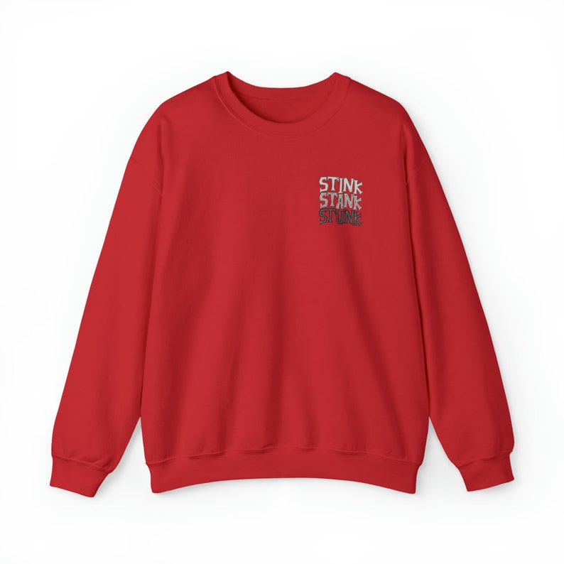 Peut inclure: Un sweat-shirt rouge avec le mot "STINK" superpos&eacute; trois fois dans une police grise vieillie sur la poitrine sup&eacute;rieure gauche. Le sweat-shirt a des manches longues et un col rond.
