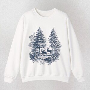 May include: White sweatshirt featuring a forest scene with two deer and tall trees in a dark blue print. The crew neck sweatshirt has long sleeves and the word "WHITE" is printed at the bottom.