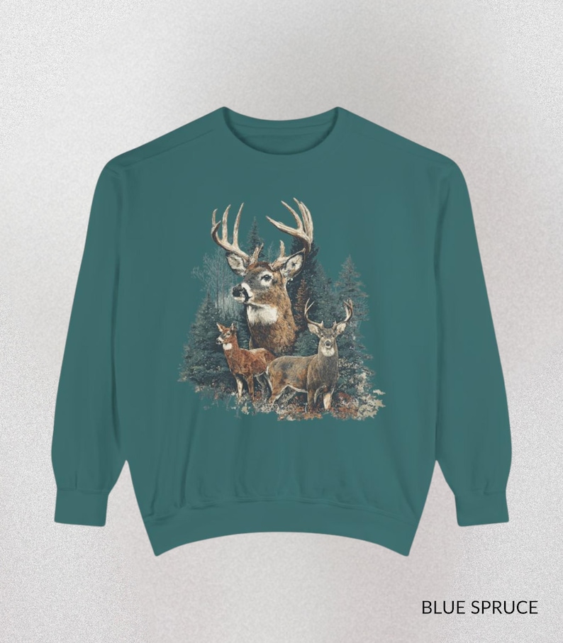 May include: Teal sweatshirt featuring a detailed illustration of three deer in a forest setting. The design includes a large buck with prominent antlers and two smaller deer. The text "BLUE SPRUCE" is printed at the bottom.