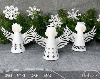 May include: Three white paper angel ornaments with different patterns on their skirts. The angels have haloes and wings. The ornaments are sitting on a gray surface.