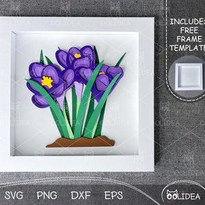 May include: A white frame with a purple and green paper flower arrangement inside. The flowers are layered and have a 3D effect. The frame includes the text "INCLUDES FREE FRAME TEMPLATE!"