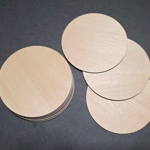 May include: A stack of unfinished, round wooden coasters. Several individual coasters are also visible. The coasters are made of light-colored wood and have a smooth surface. They are suitable for DIY projects or home decor.
