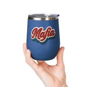 May include: A blue insulated tumbler with a silver rim and lid. The tumbler features the word "Mafia" in a retro red and white design. The tumbler is held by a hand against a white background.