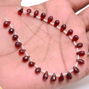 Può includere: Una collana di perle di pietra preziosa rosso scuro a forma di goccia. Le perle sono infilate su un filo d'argento.
