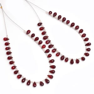 May include: Two strands of red gemstone beads, each strand is strung on a silver wire and features teardrop-shaped beads.