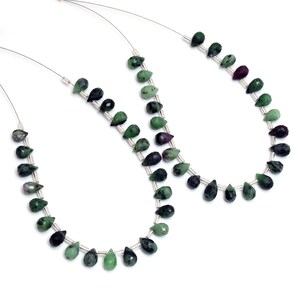 Könnte beinhalten: Zwei Stränge grüner und schwarzer Edelsteinperlen, die auf silbernem Draht aufgefädelt sind. Die Perlen haben die Form eines Tropfens.