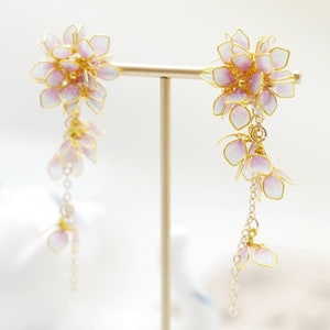 May include: A pair of dangle earrings with a cluster of pink and white flowers at the top and a chain of smaller flowers hanging down.