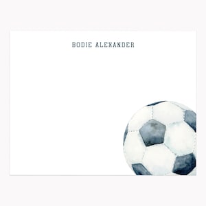 May include: White stationery with the name "BODIE ALEXANDER" in navy blue. A watercolor soccer ball in shades of gray and white is in the lower right corner. The stationery is perfect for personalized notes.