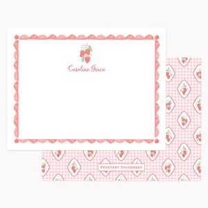 May include: A white rectangular stationery card with a pink scalloped border, a strawberry illustration, and the text Caroline Grace. Beneath it, a matching pink and white gingham patterned paper features diamond shapes with strawberries.