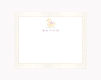 May include: A rectangular stationery card featuring a light yellow duck illustration with a pink ribbon around its neck. Below the duck, the text BABY EVELYN is printed in pink. The card has a thin, light-colored striped border frame.