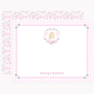May include: Pink stationery set featuring a Barbie theme. The design includes a pink gingham border, floral accents, and a central illustration of a blonde-haired girl within a floral wreath. The name "Georgia Roberts" is printed at the bottom.