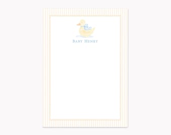 May include: A rectangular stationery card featuring a pale yellow duck illustration with a light blue ribbon around its neck. Below the duck, the text BABY HENRY is printed in blue. The card has a white center and a light beige striped border.