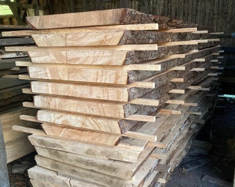 Op de afbeelding: Een stapel houten planken, waarschijnlijk voor houtbewerkingsprojecten, zijn gestapeld in een schuur. De planken zijn lichtbruin en hebben een natuurlijke houtnerf. De planken zijn gestapeld in een nette stapel, met de uiteinden van de planken uitgelijnd.